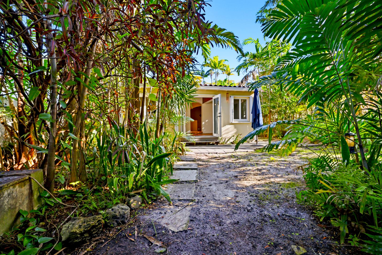 Backyard path leading toward the house through dense tropical landscaping